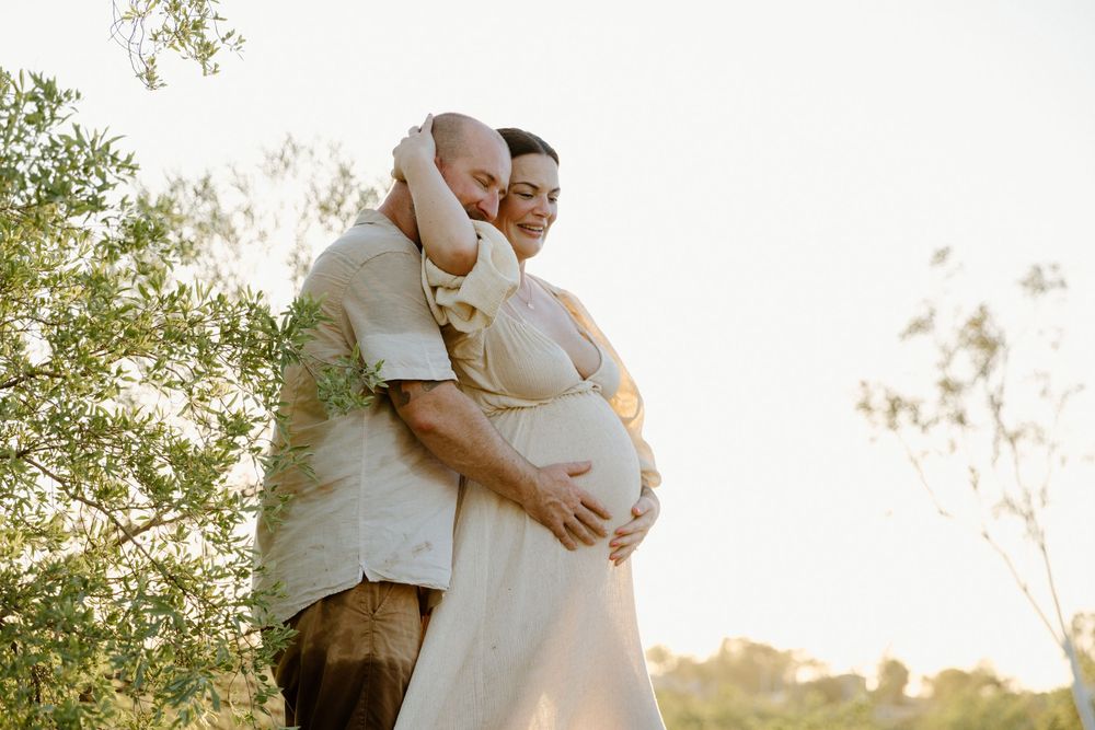 A couple in light colored clothing embraces tenderly during a sunset outdoor photo session.