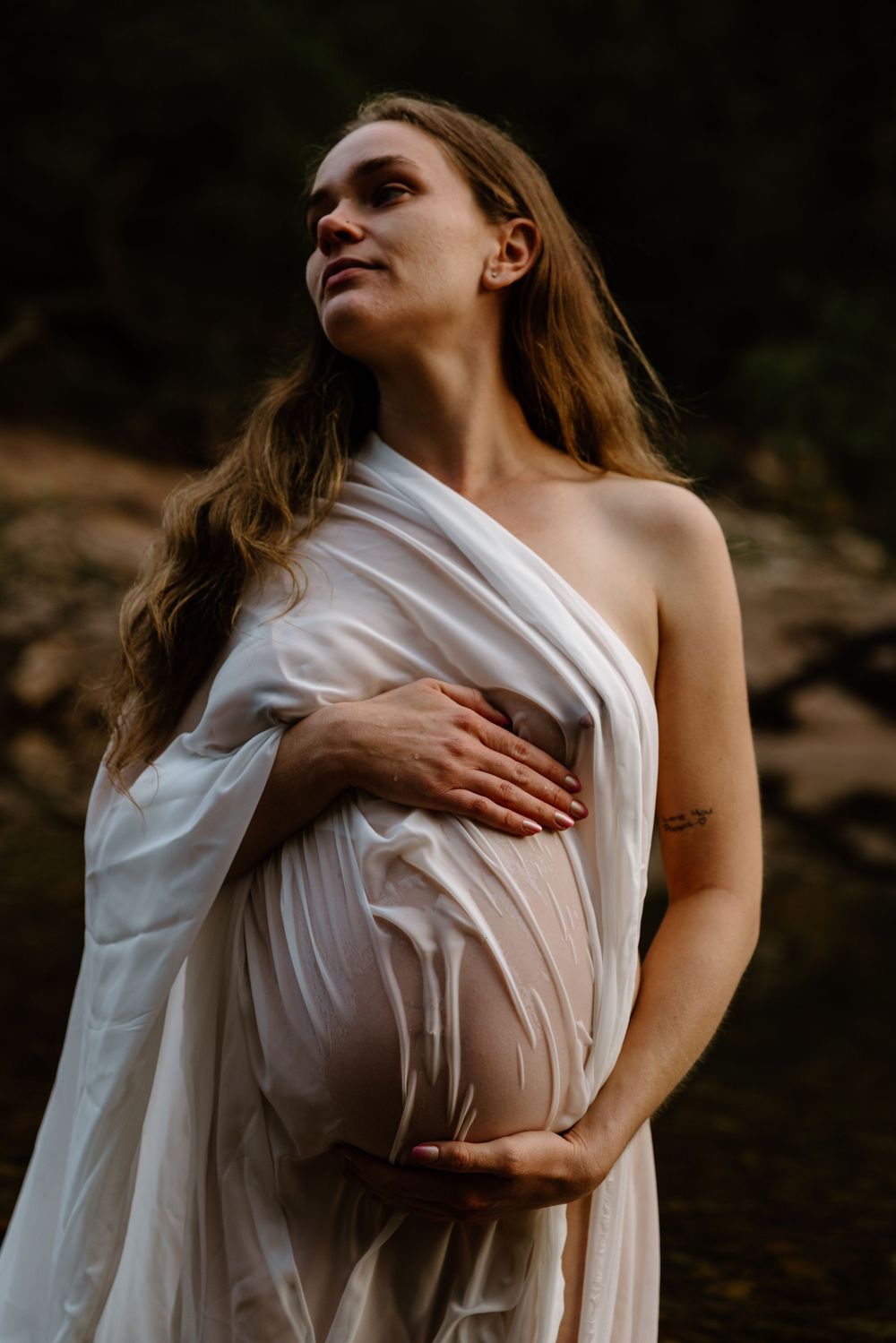 A person wrapped in flowing white fabric poses thoughtfully against a dark background in an artistic portrait.