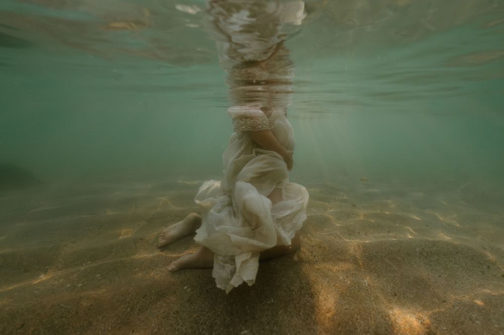 Underwater view of flowing white fabric against sandy bottom in turquoise water.
