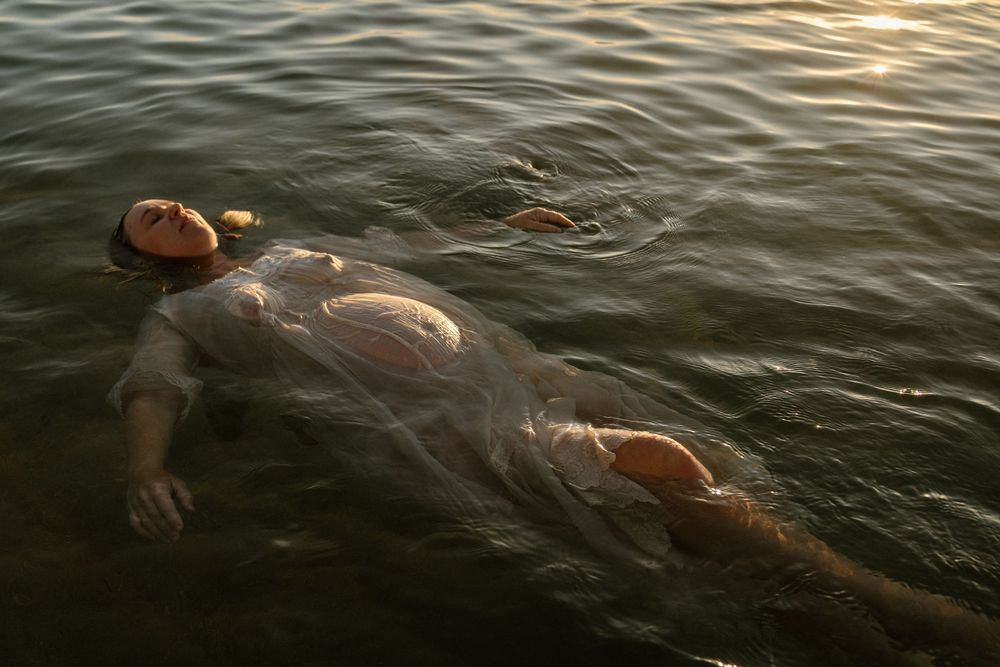 Gentle ripples in dark water catch the golden light of sunset while swimmers enjoy an evening dip.