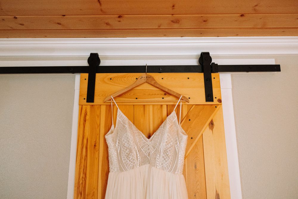A white lace wedding dress hangs on a rustic wooden barn door with black sliding hardware.