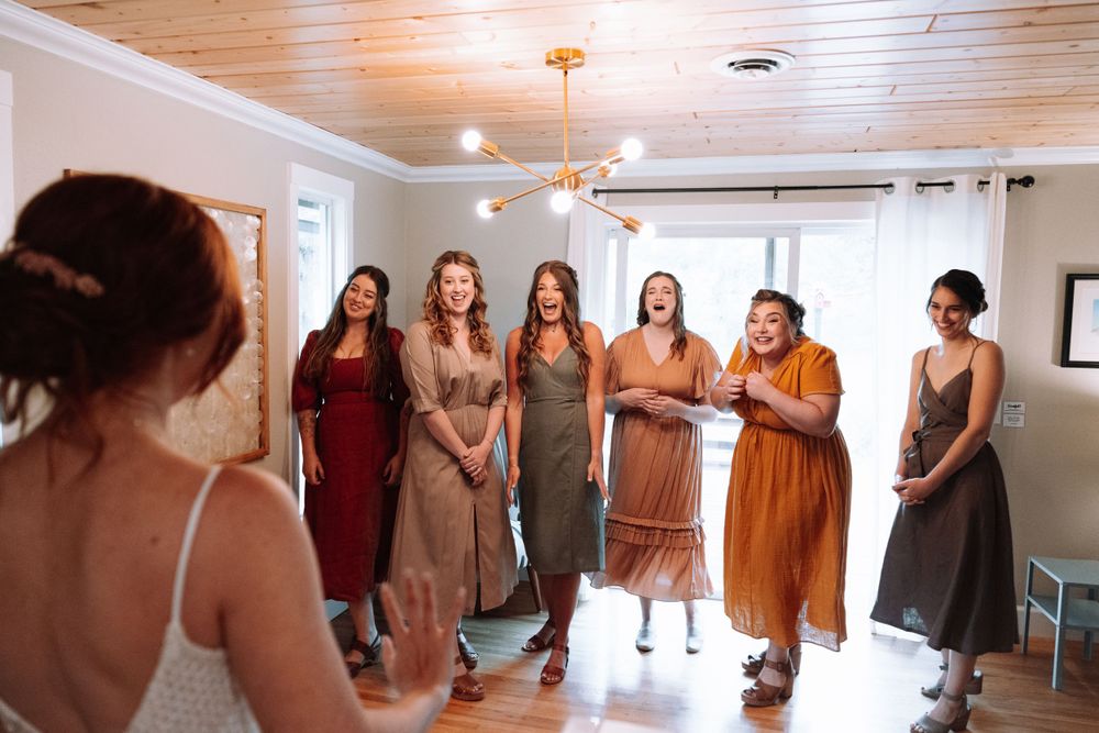 Bridesmaids in varying shades of autumn dresses stand together in a bright room with wooden ceilings.