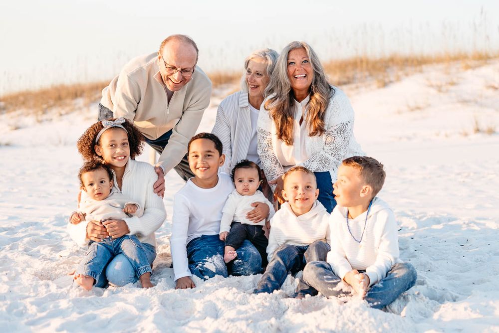 Kids playing on the beach while grand parents lean down to join in on the fun.