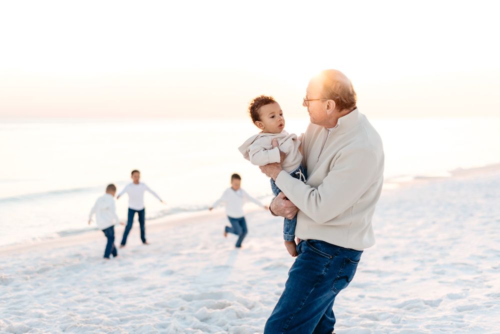 Grandfather holding his grandchild as the children play along the beaches of Destin Florida