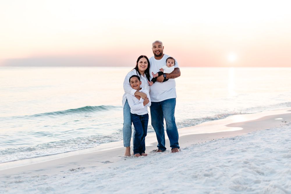 Cute small family posing for pictures during a beautiful gold and orange sunset in Fort Walton Beach Florida