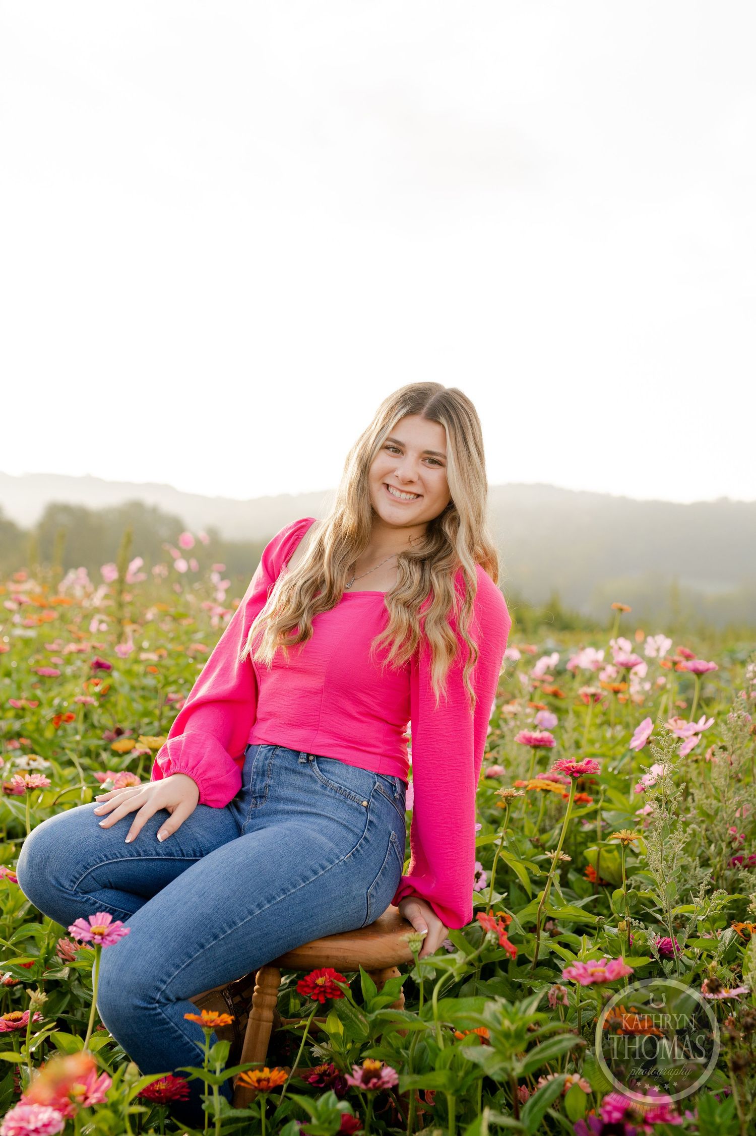 Casual outdoor portrait wearing bright pink sweater and jeans while sitting among blooming flowers.