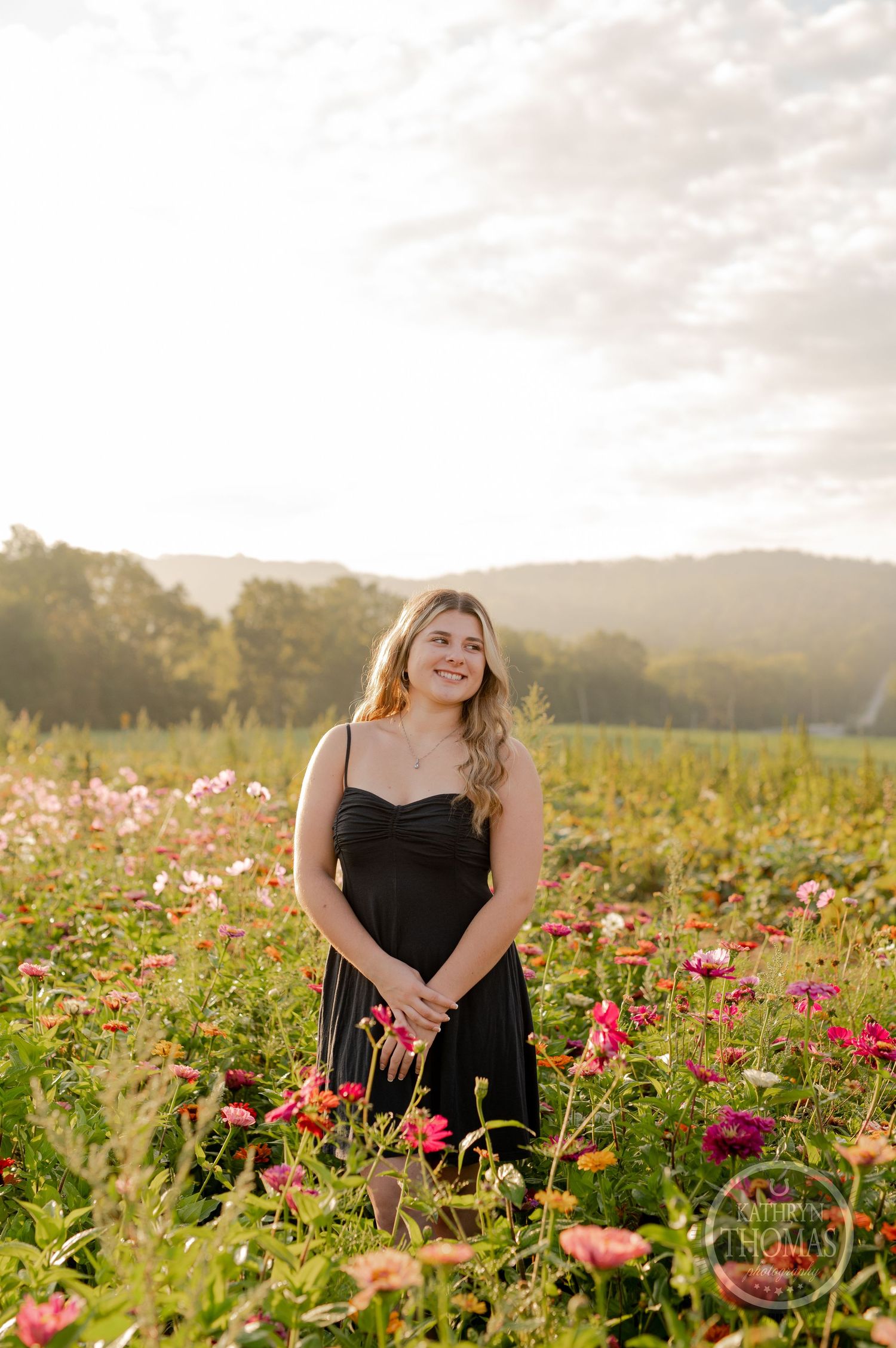 Portrait surrounded by colorful cosmos flowers in a meadow during sunset with mountains in the distance.