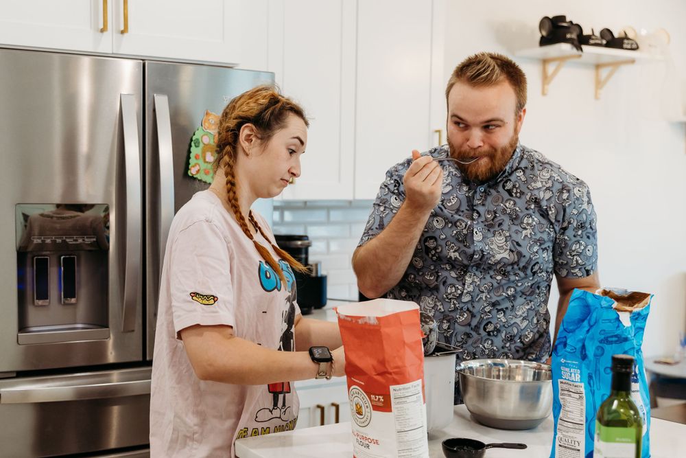 Two people taste-testing ingredients while cooking together in a modern kitchen.