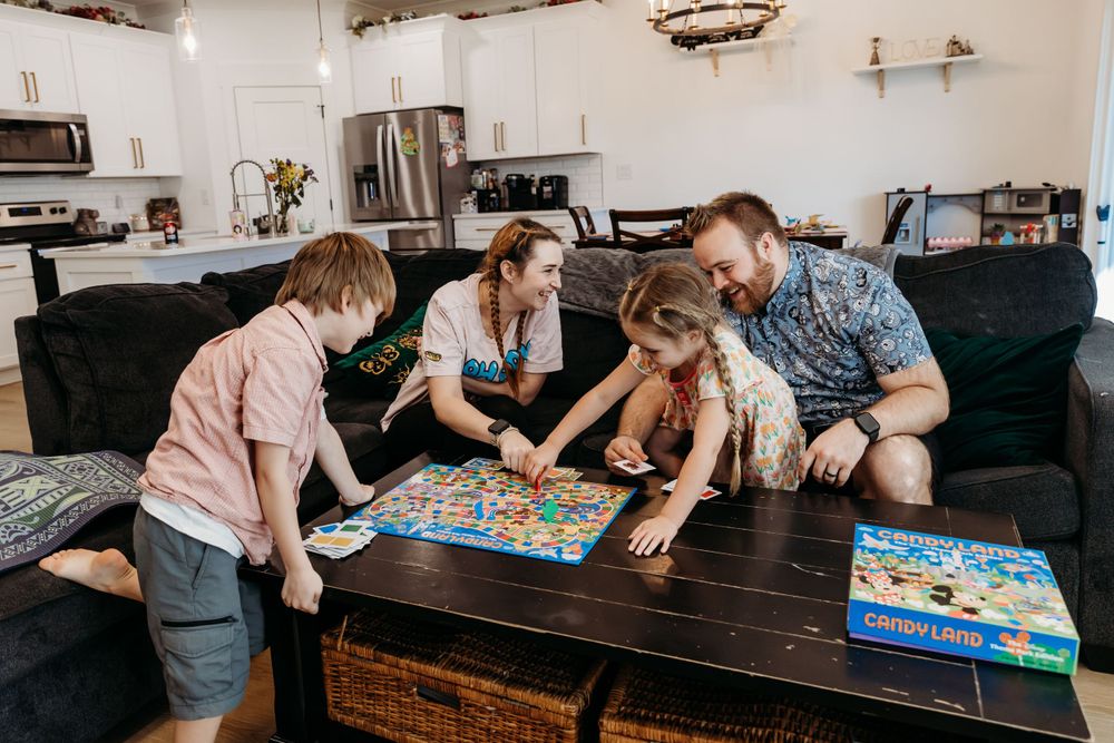 Family gathered around a dark wooden table playing board games together.