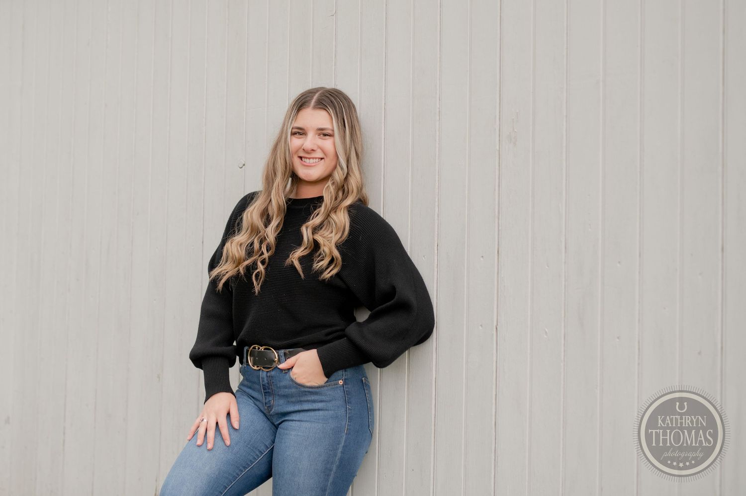 Stylish casual portrait against white wall wearing cropped black sweater and blue jeans.