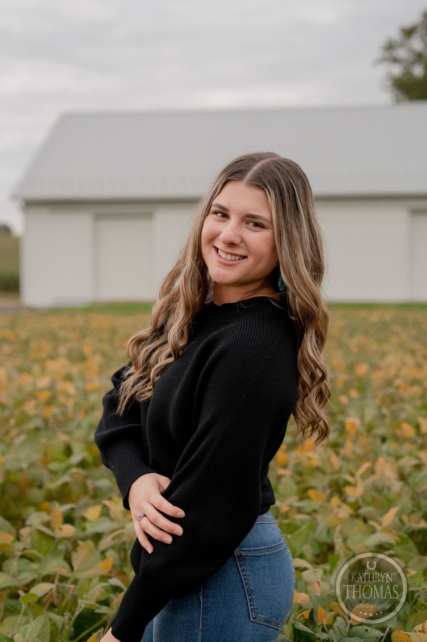 Casual autumn portrait session against rustic white barn and pumpkin patch backdrop.