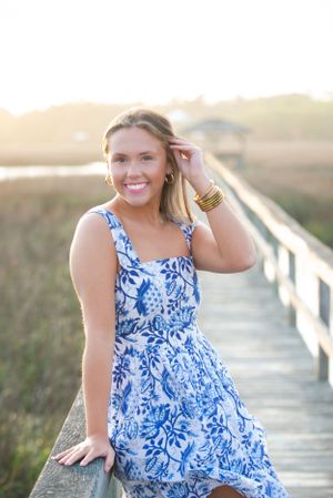 A summer portrait in a blue floral dress on a wooden boardwalk at sunset.