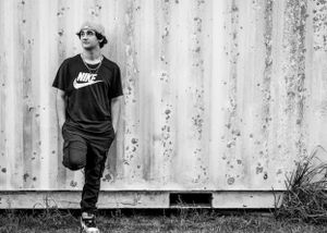 Black and white portrait of someone in Nike shirt leaning against a corrugated wall.