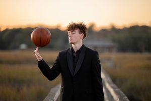 A formal portrait balancing a basketball against a sunset backdrop.