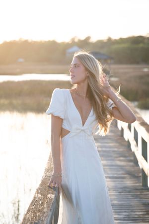 A person in a white dress poses on a wooden boardwalk during golden hour.