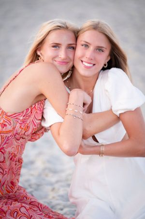 Two people in summer dresses embrace while posing on a beach during sunset.