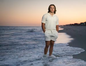 Person in white outfit standing in ocean waves at sunset on sandy beach.