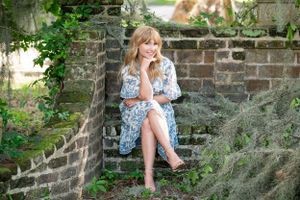 A person in a patterned dress sits relaxed on old brick steps covered with moss and greenery.