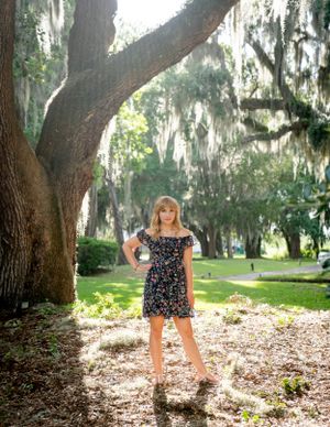 A person poses beneath a large oak tree draped with Spanish moss in a Southern garden setting.
