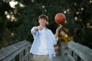 Person in casual attire poses with basketball on wooden bridge outdoors.