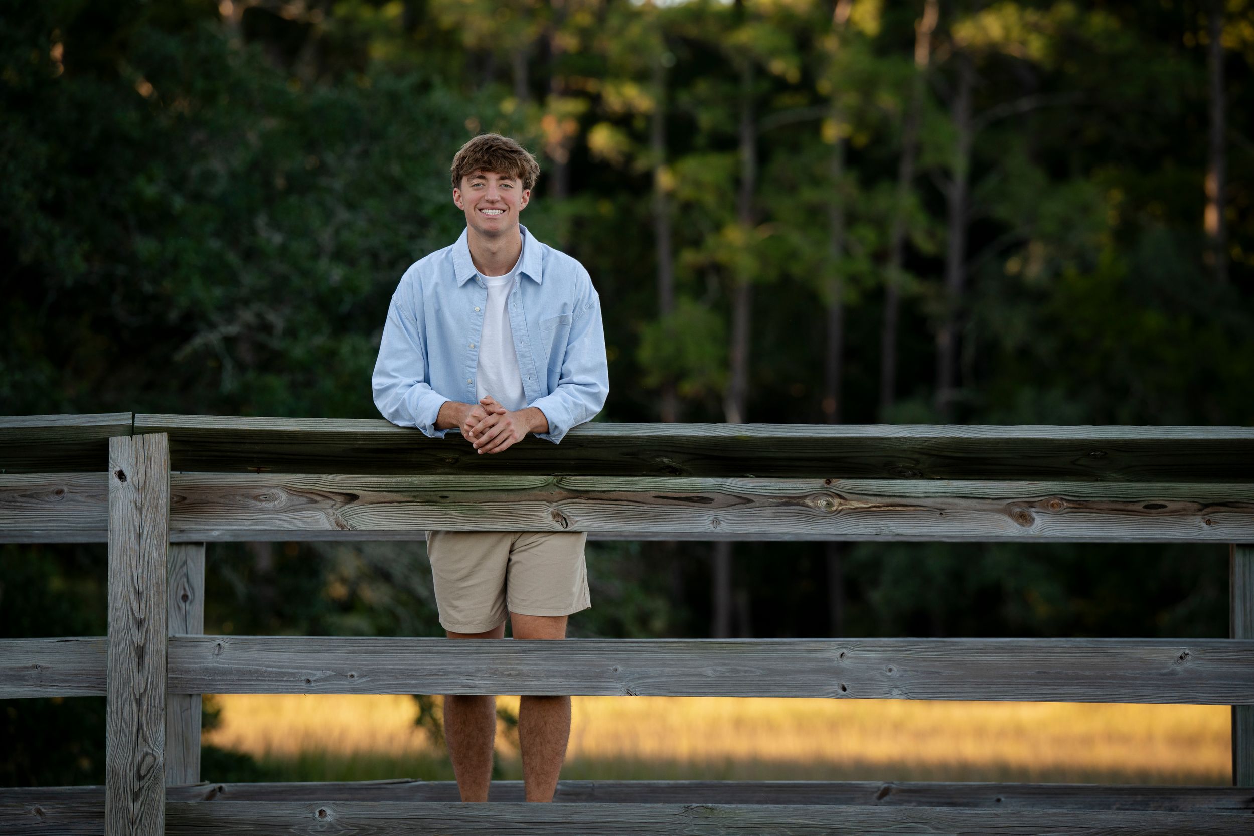 Young person stands casually on wooden bridge during sunset.
