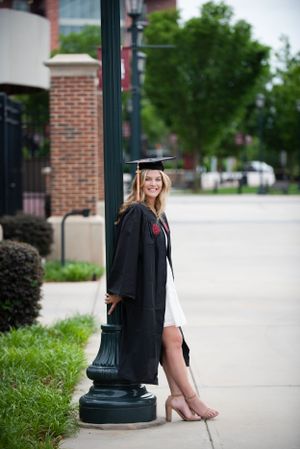 Graduation portrait in cap and gown leaning against vintage lamp post.