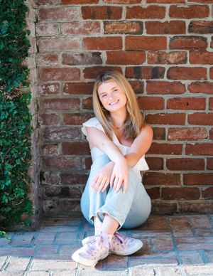 Casual portrait against a brick wall with ivy and pink sneakers.