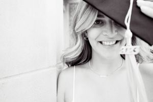 A black and white portrait showing a bright smile under an umbrella.