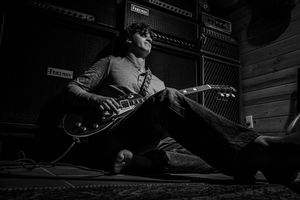 Black and white photo of a guitarist performing on stage with dramatic lighting and shadows.