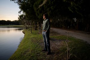 Silhouetted figures stand along a lakeside path at sunset creating a peaceful outdoor scene.