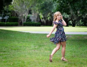A person in a floral dress runs playfully across a sunny green lawn.