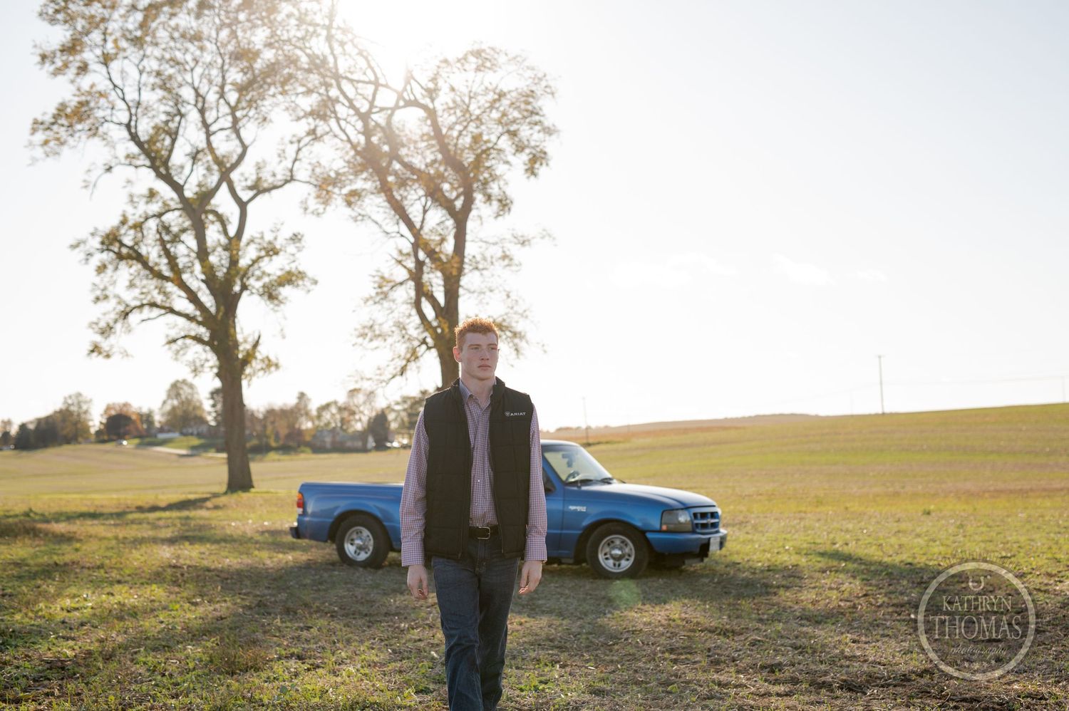 A classic blue car parked near trees in an autumn field.