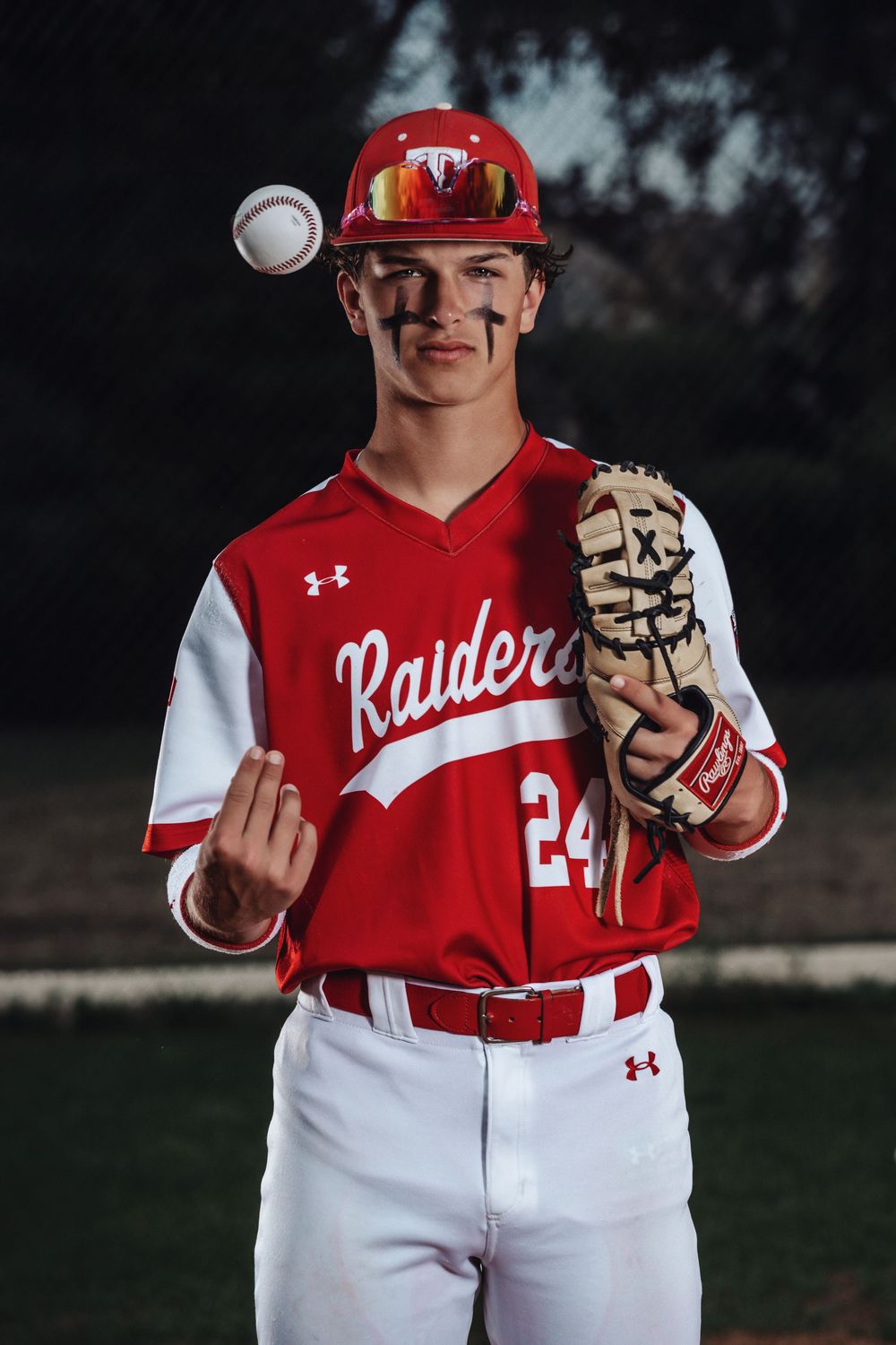Baseball player in red Raiders jersey #24 poses with ball and glove against dark background.