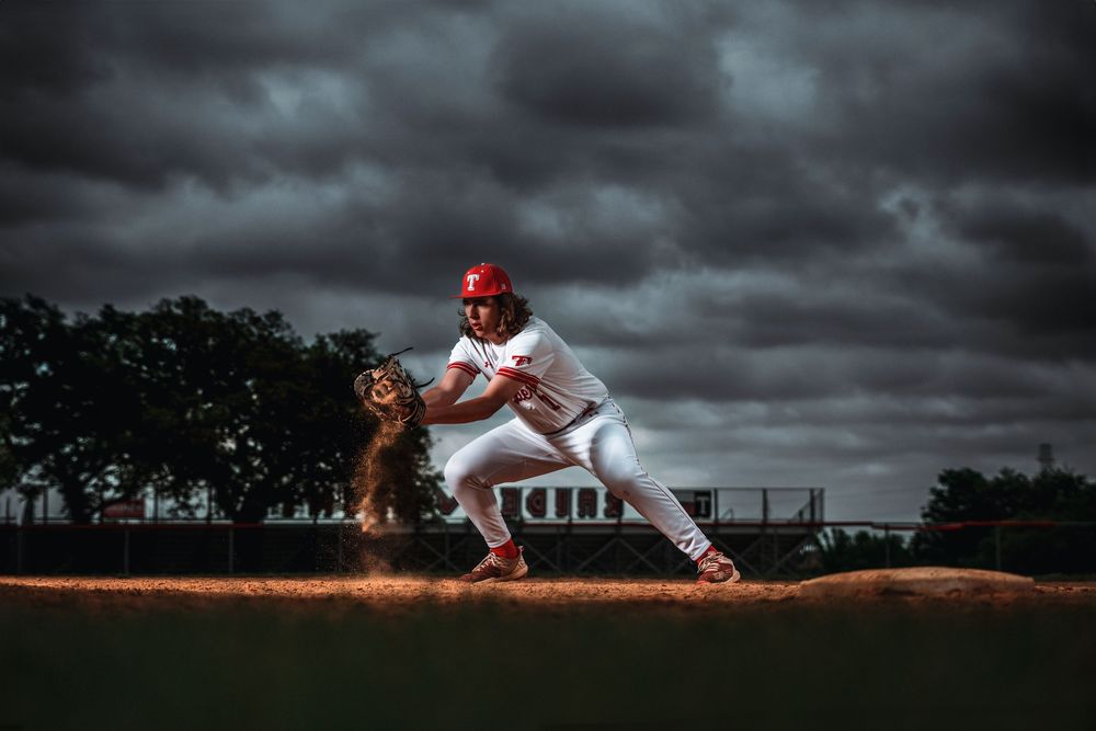 Dramatic baseball pitcher throwing from mound against dark stormy sky with dirt flying in dramatic lighting.