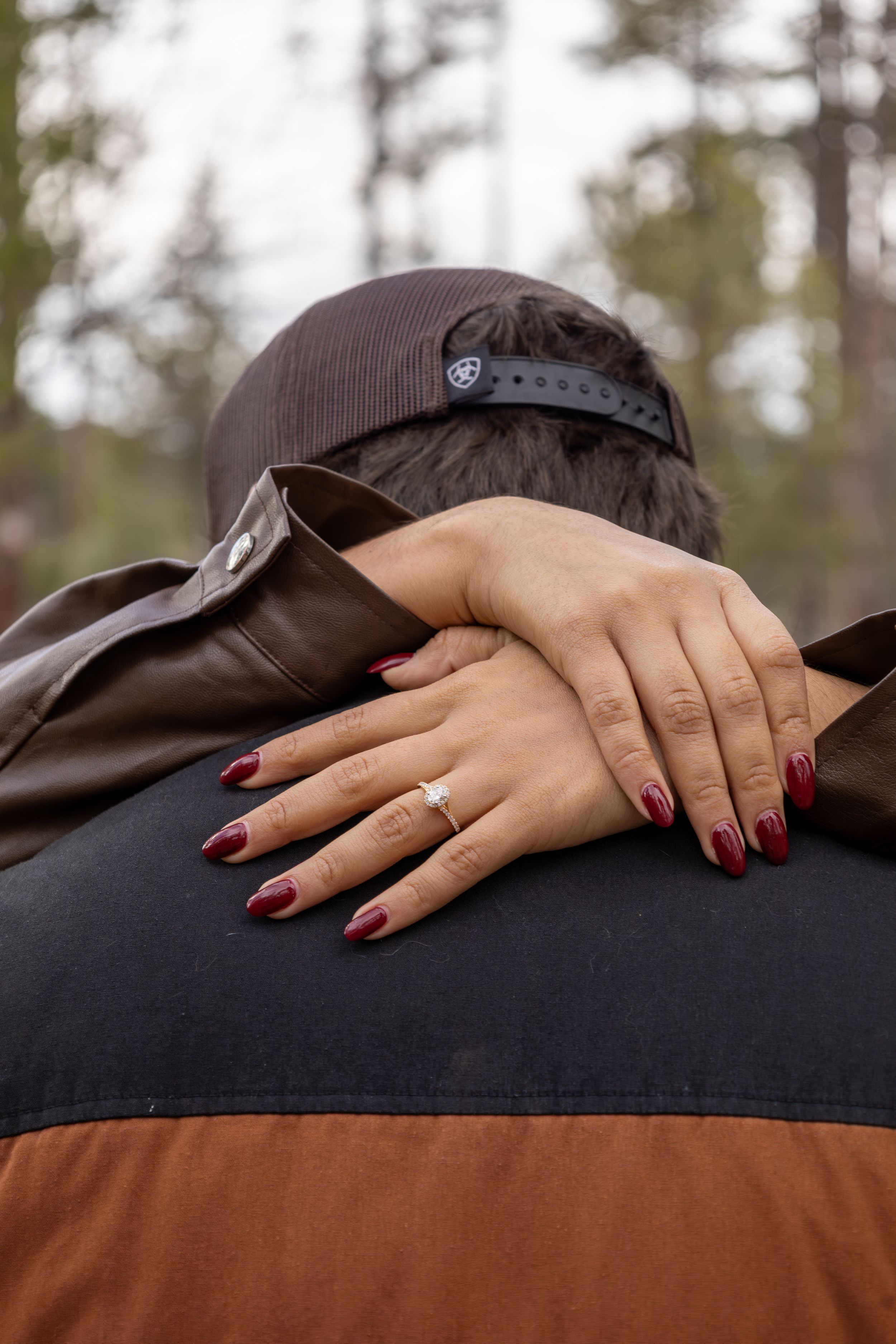 Woman with red nails and engagement ring embracing man outdoors.