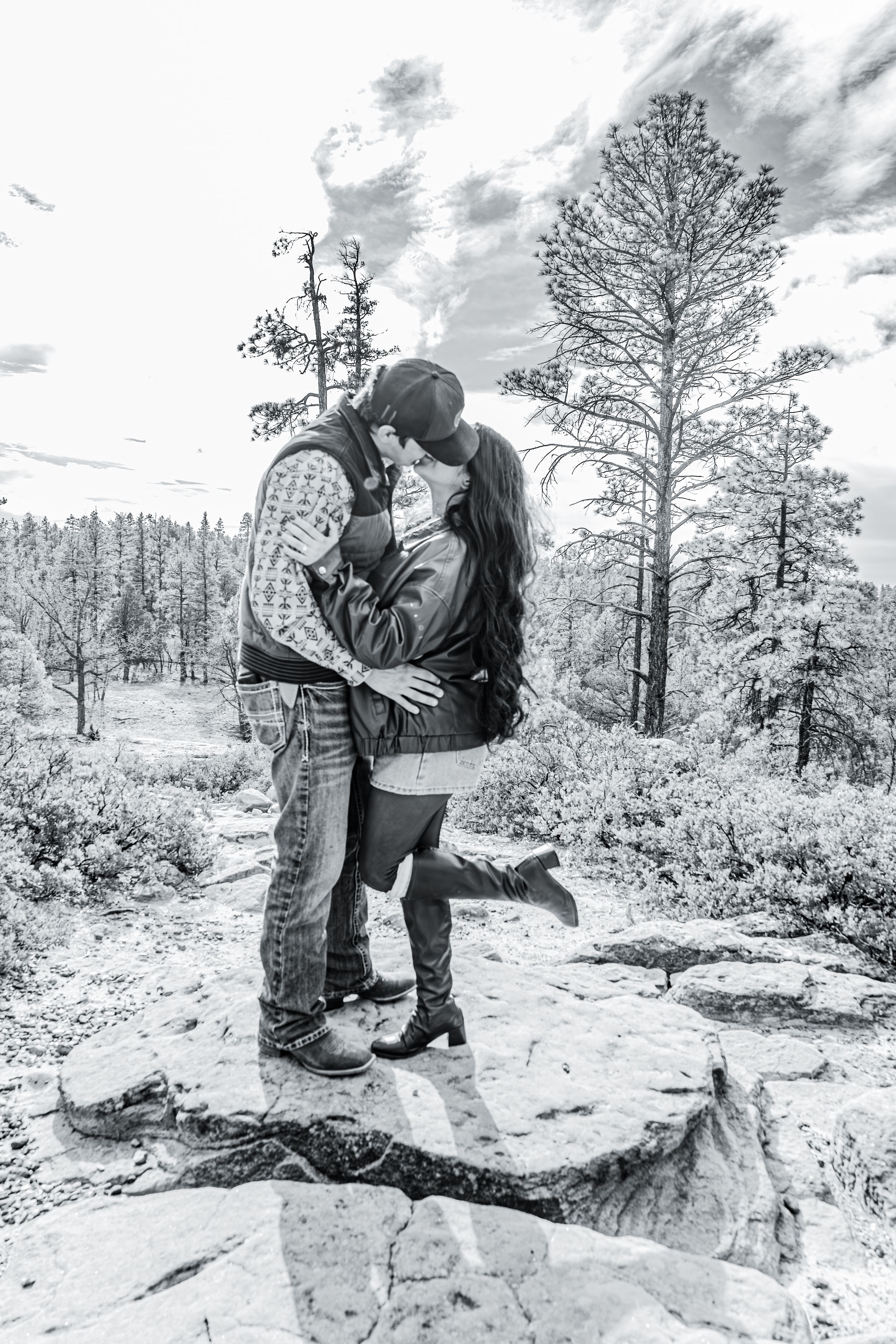Black and white photo of couple kissing on rocks in forest.