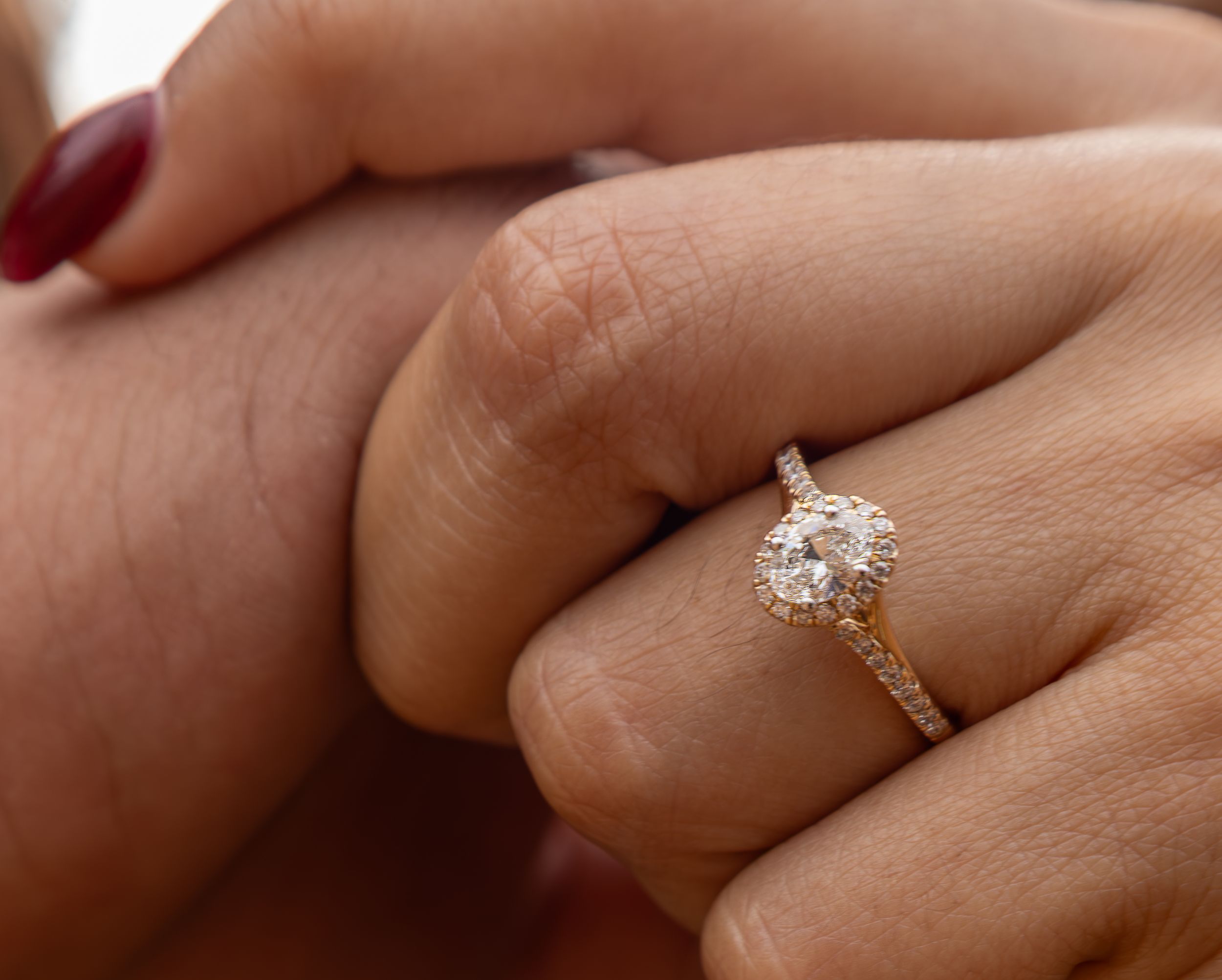 Close-up of an oval diamond halo engagement ring on a woman's finger.