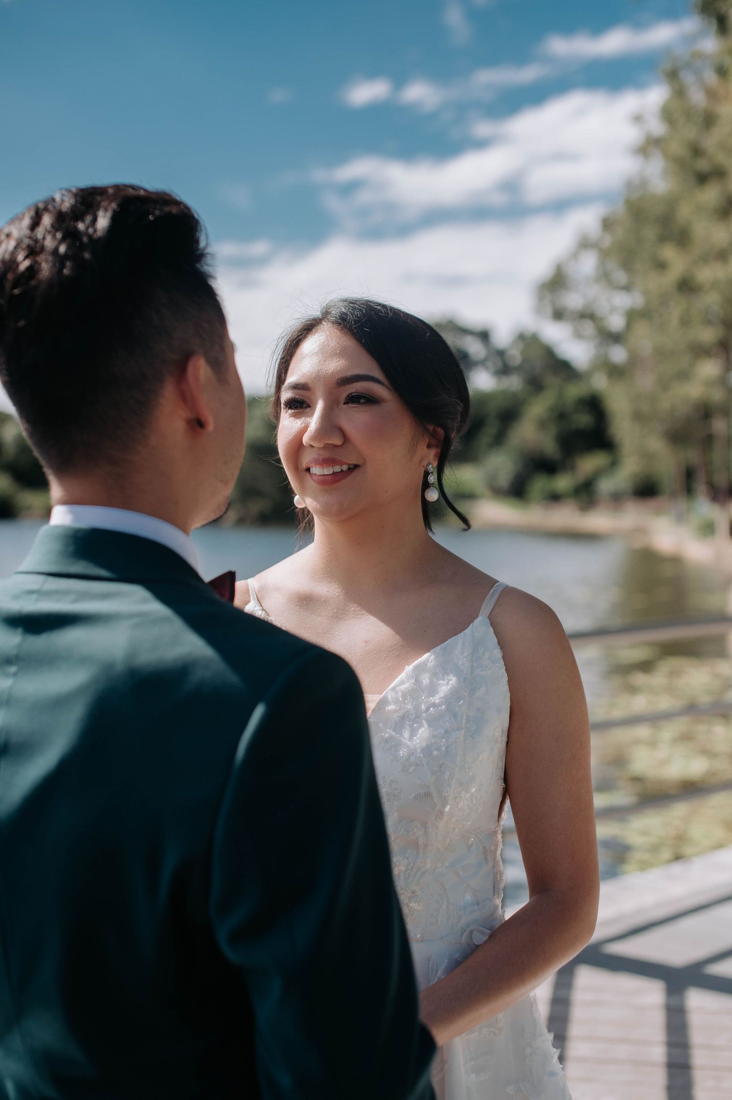 A couple shares an intimate moment on a lakeside dock with a flowing white wedding dress trailing behind them.