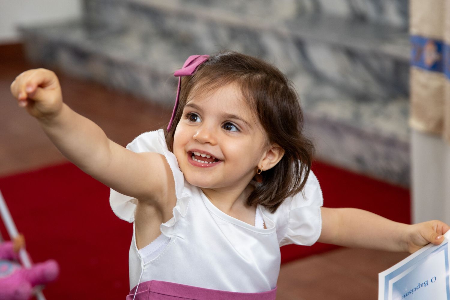 Young child in white shirt joyfully raising arms during celebration.