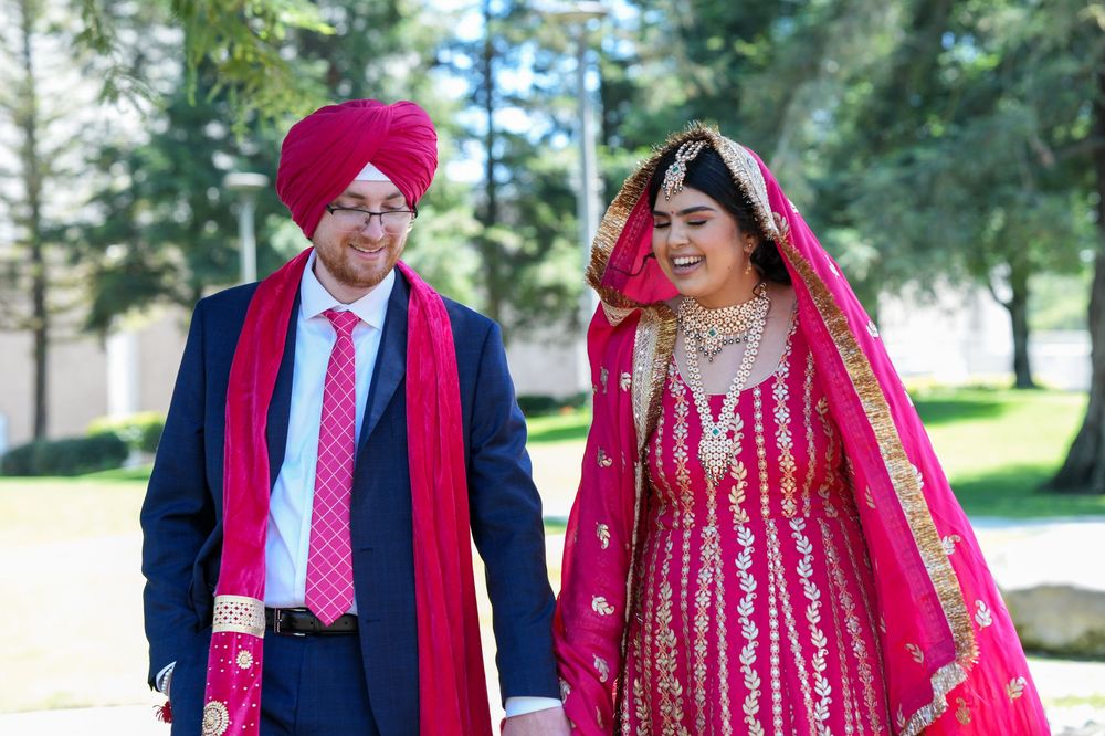 A couple in traditional Indian wedding attire walking together outdoors in a park setting on a sunny day.