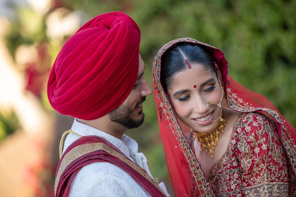 Traditional Sikh wedding couple in red and gold attire share a tender moment during their outdoor ceremony.