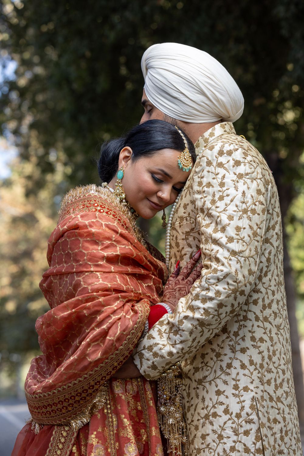 Intimate moment between couple in traditional Indian wedding attire with gold and coral colored outfits.