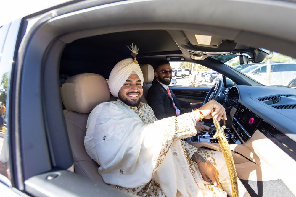 Two occupants sit in a luxury vehicle interior with beige leather seats, as sunlight streams through the windshield.