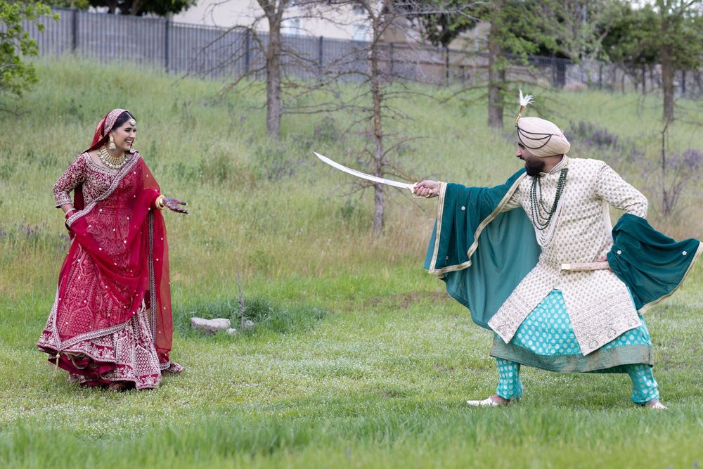 Two dancers in traditional South Asian attire perform outdoors on grass, one in red and one in turquoise striking dynamic poses.