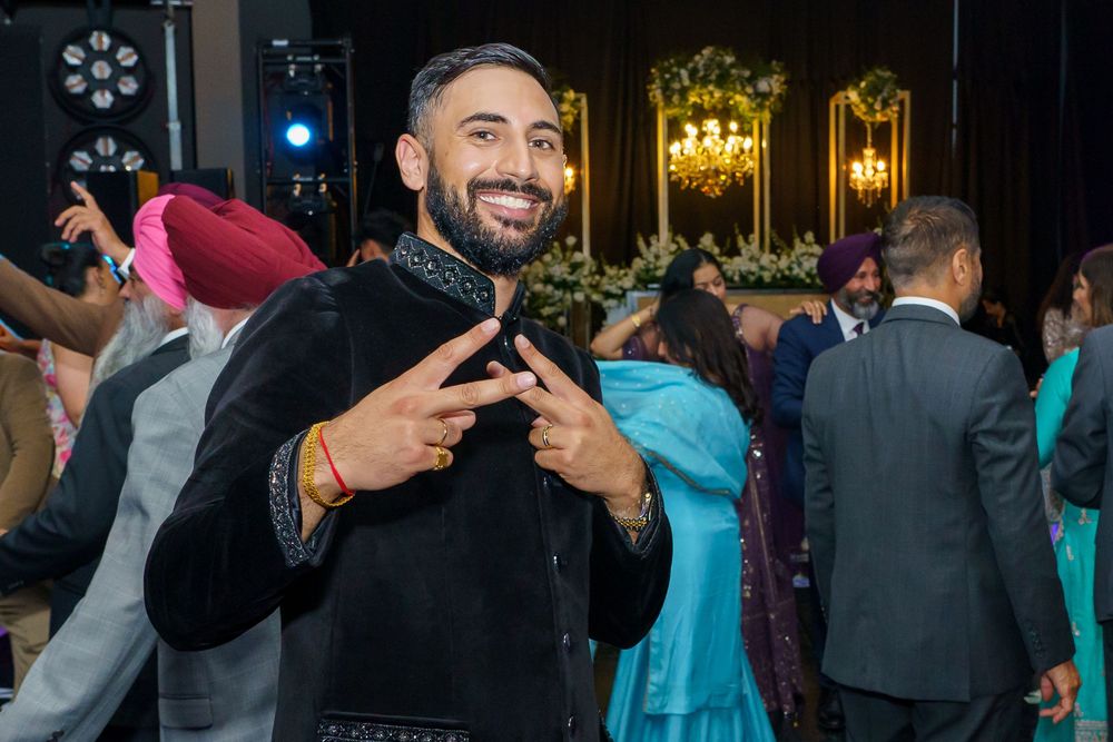 A person in a dark outfit makes a peace sign gesture while smiling at a formal party.