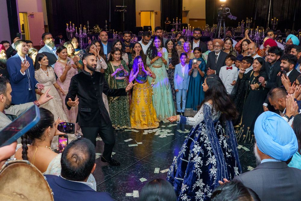 Celebratory crowd gathers around dancers at a festive Indian wedding reception with colorful traditional attire and decor.