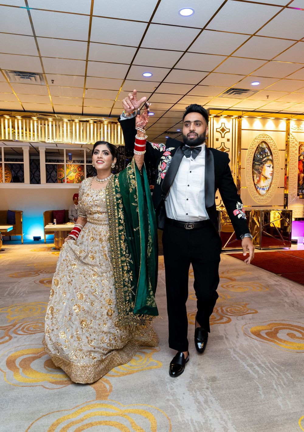 A couple in formal attire walks through an elegant reception venue decorated with golden accents and lighting.