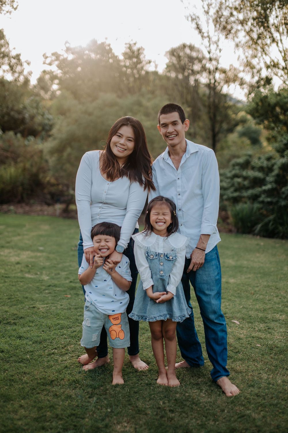 A family of four poses together on a grassy lawn during golden hour.