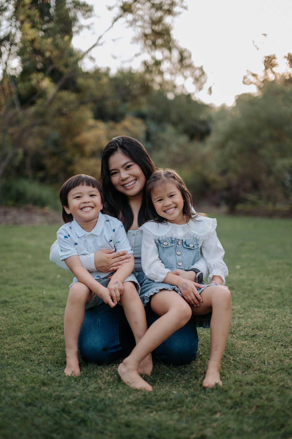 Three people in coordinating denim outfits sitting together on green grass during sunset photo session.