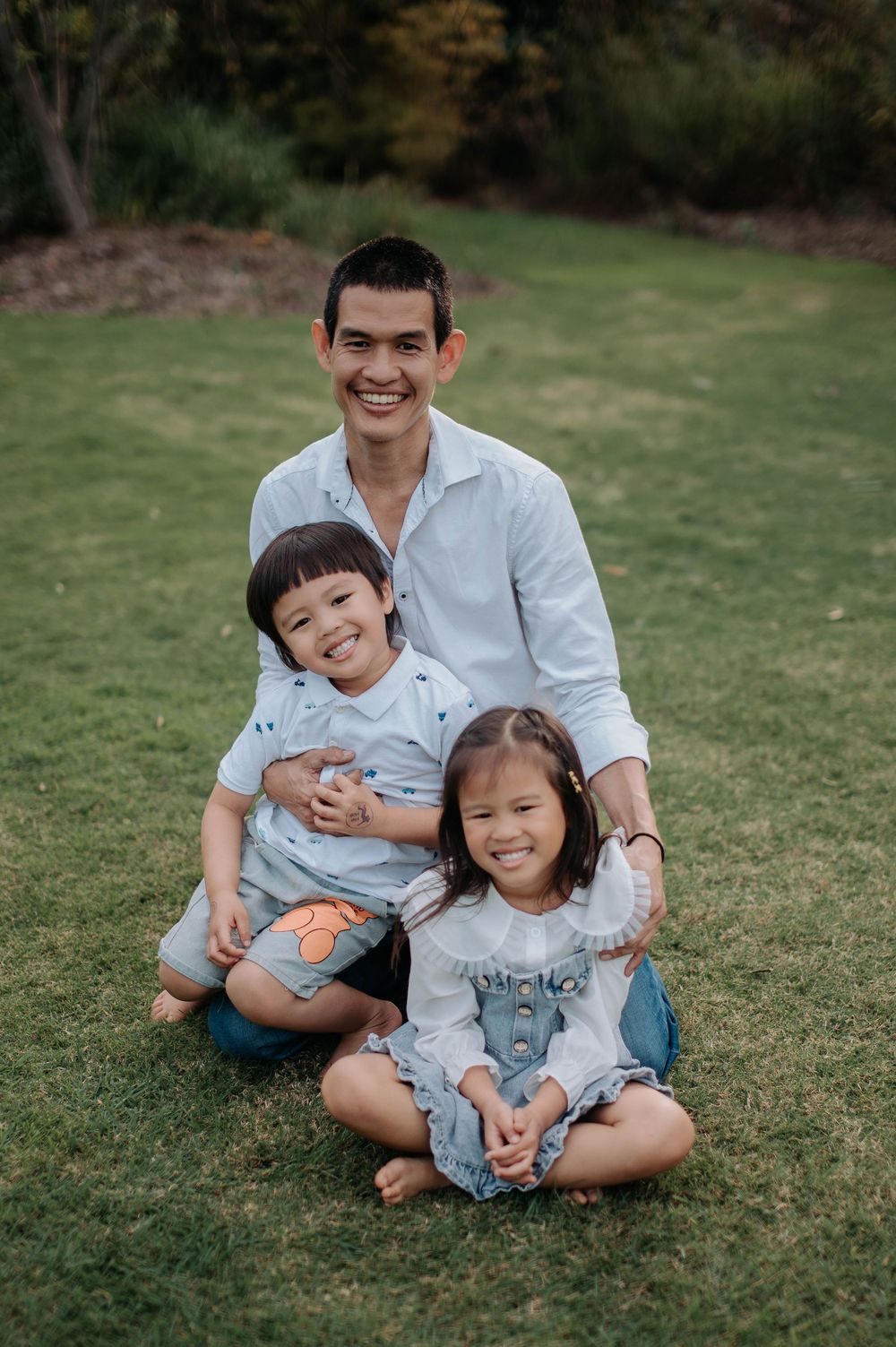 Three people sit together on grass during an outdoor portrait session.